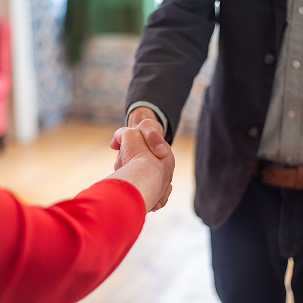 A woman in a red sweater and a man in a dark suit shake hands.