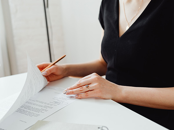White woman in a black dress and gold jewellery signing a contract with a pen